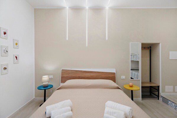 Ein modernes Hotelzimmer mit Bett, Nachttischen, einem Kleiderschrank und einem kleinen Tisch mit Lampe.