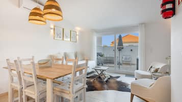 A dining area with a wooden table and chairs, a small side table, and a glass partition.