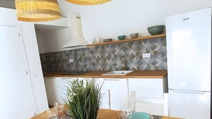 A modern kitchen with a wooden table, two hanging wicker pendant lights, a built-in sink, and a white refrigerator. - Casa Lusitano With Jacuzzi by Valada Village (Valada)