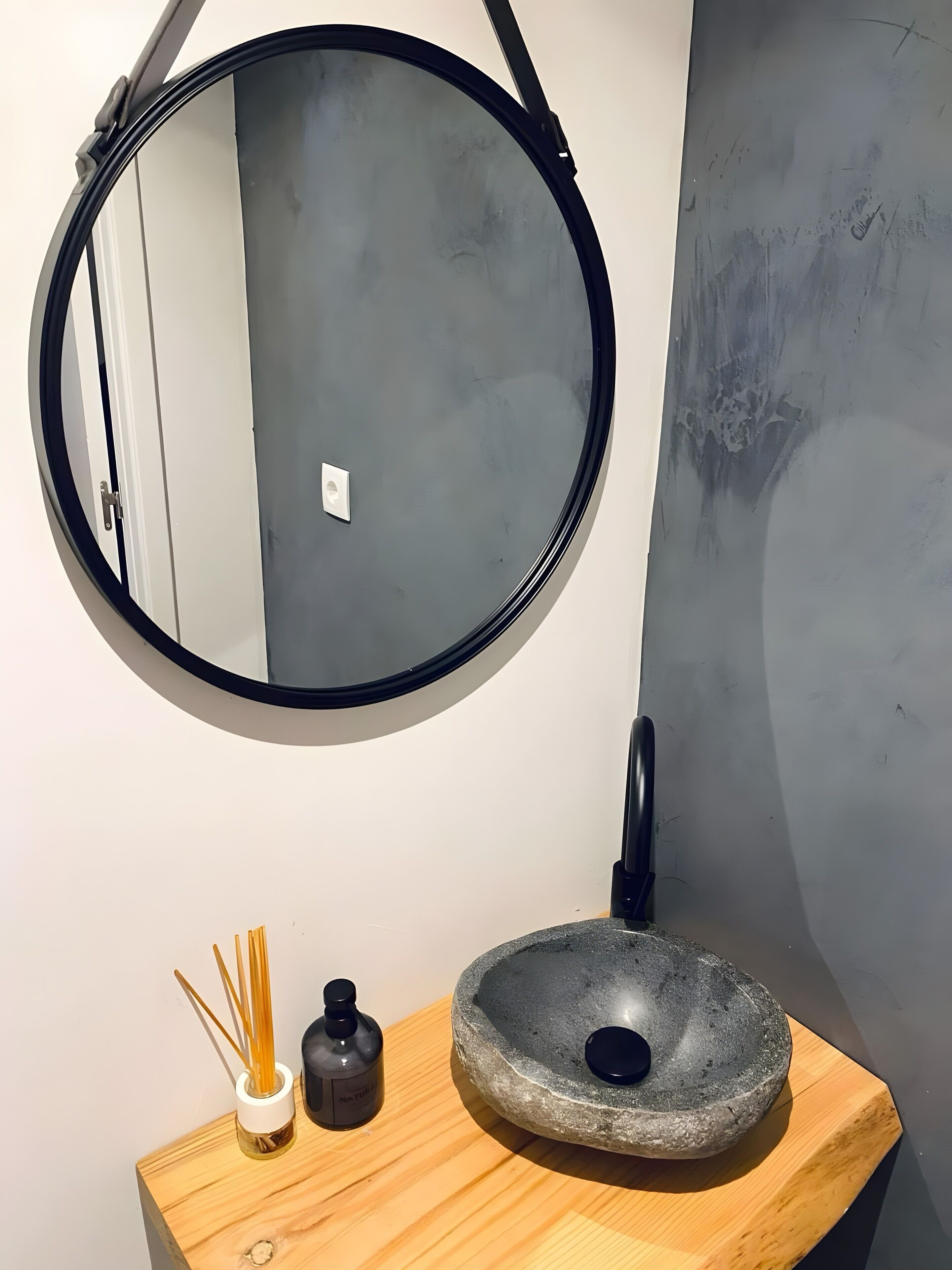 Een badkamer met een ronde spiegel, een stenen wastafel en een kleine zeepfles.