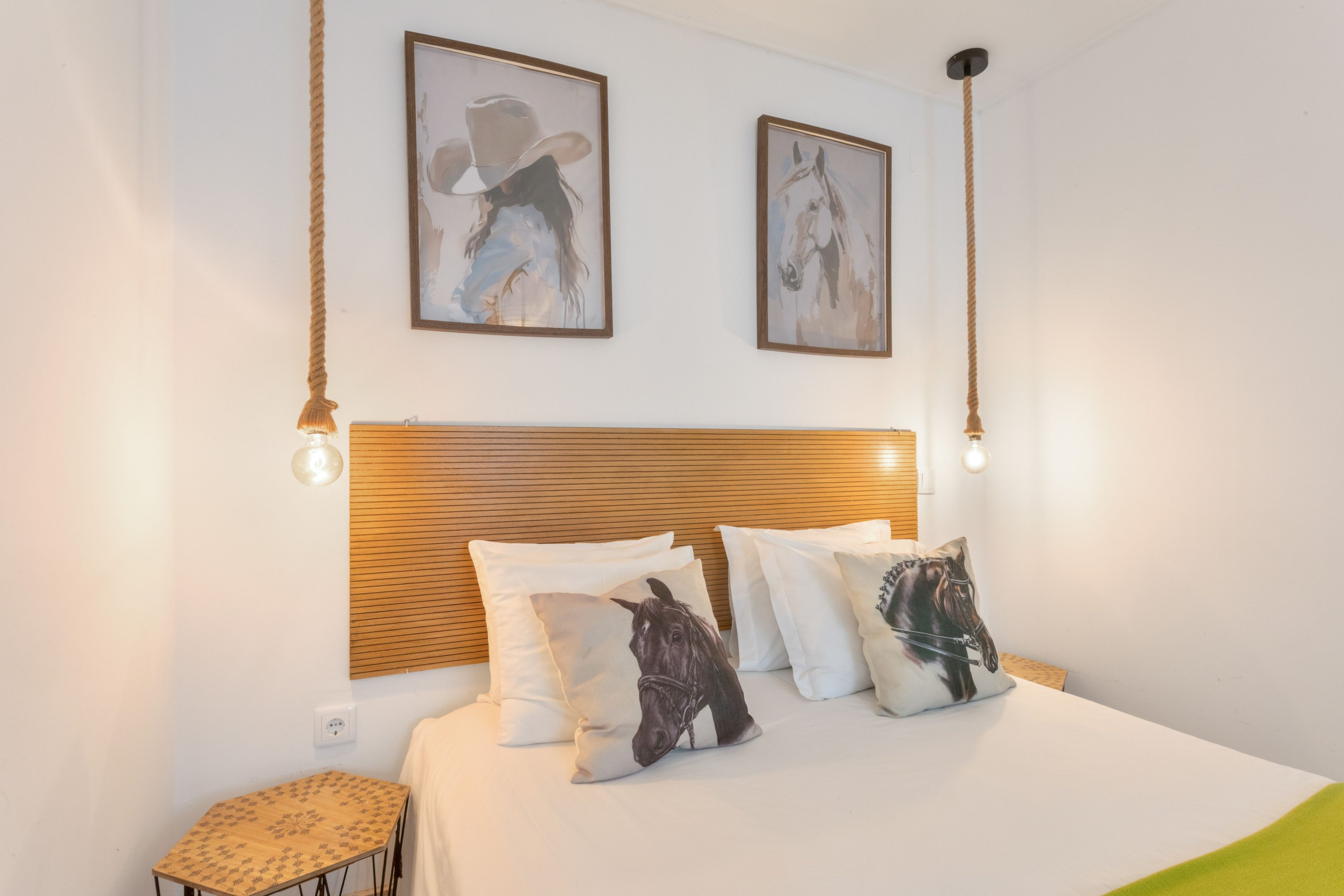 Quarto com cabeceira de madeira, duas pinturas penduradas na parede e vários travesseiros com estampas de cavalos.