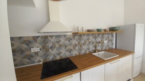 A kitchen with a geometric backsplash, a black induction cooktop, a white sink, and a built-in oven.