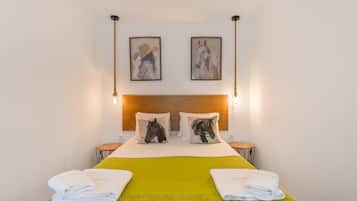 A hotel room with a bed, two pillows, two wall-mounted paintings, and two bedside lamps.