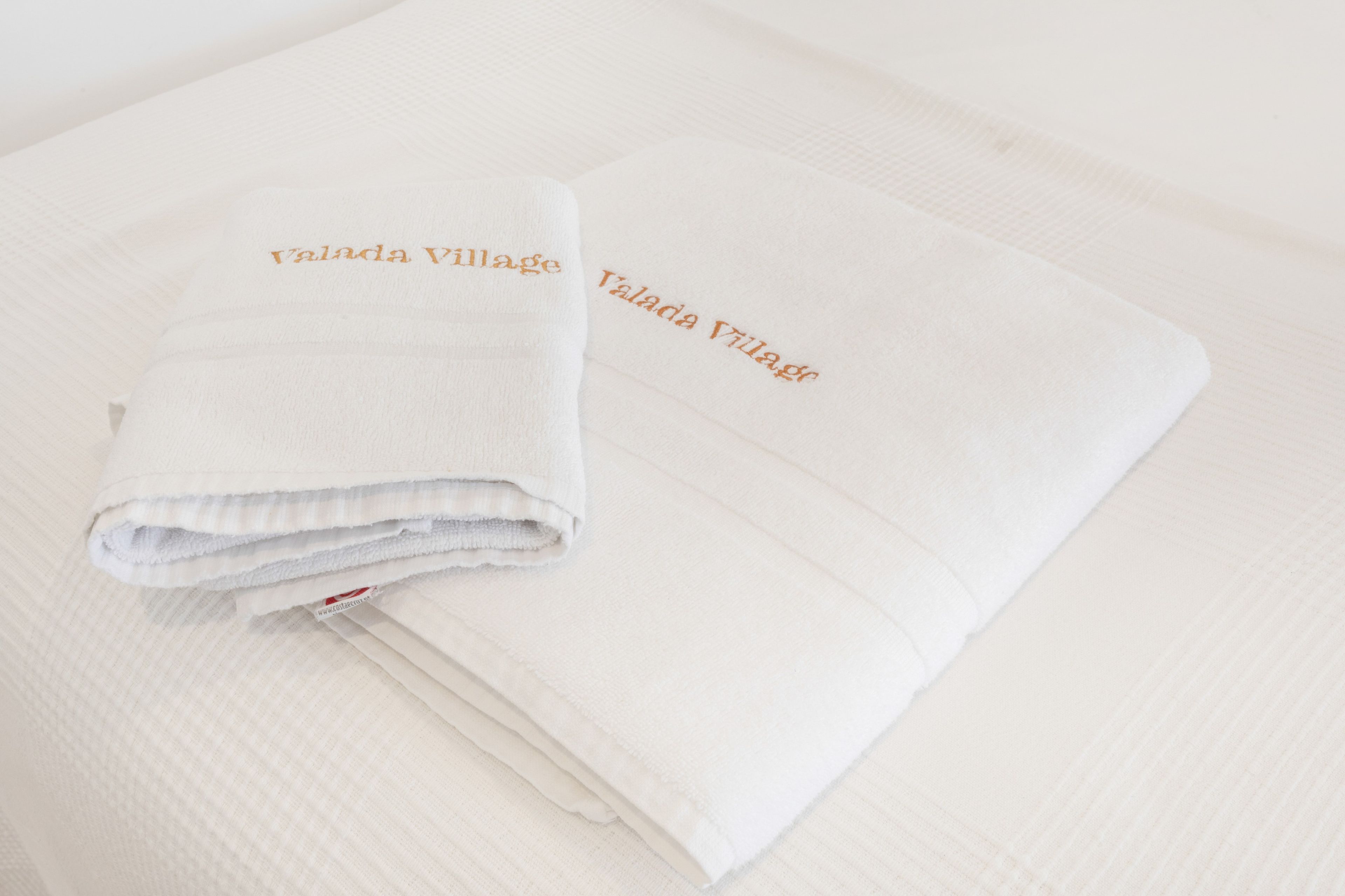 Una toalla blanca doblada con el nombre 'Valada Village' bordado, sobre una superficie blanca con textura.