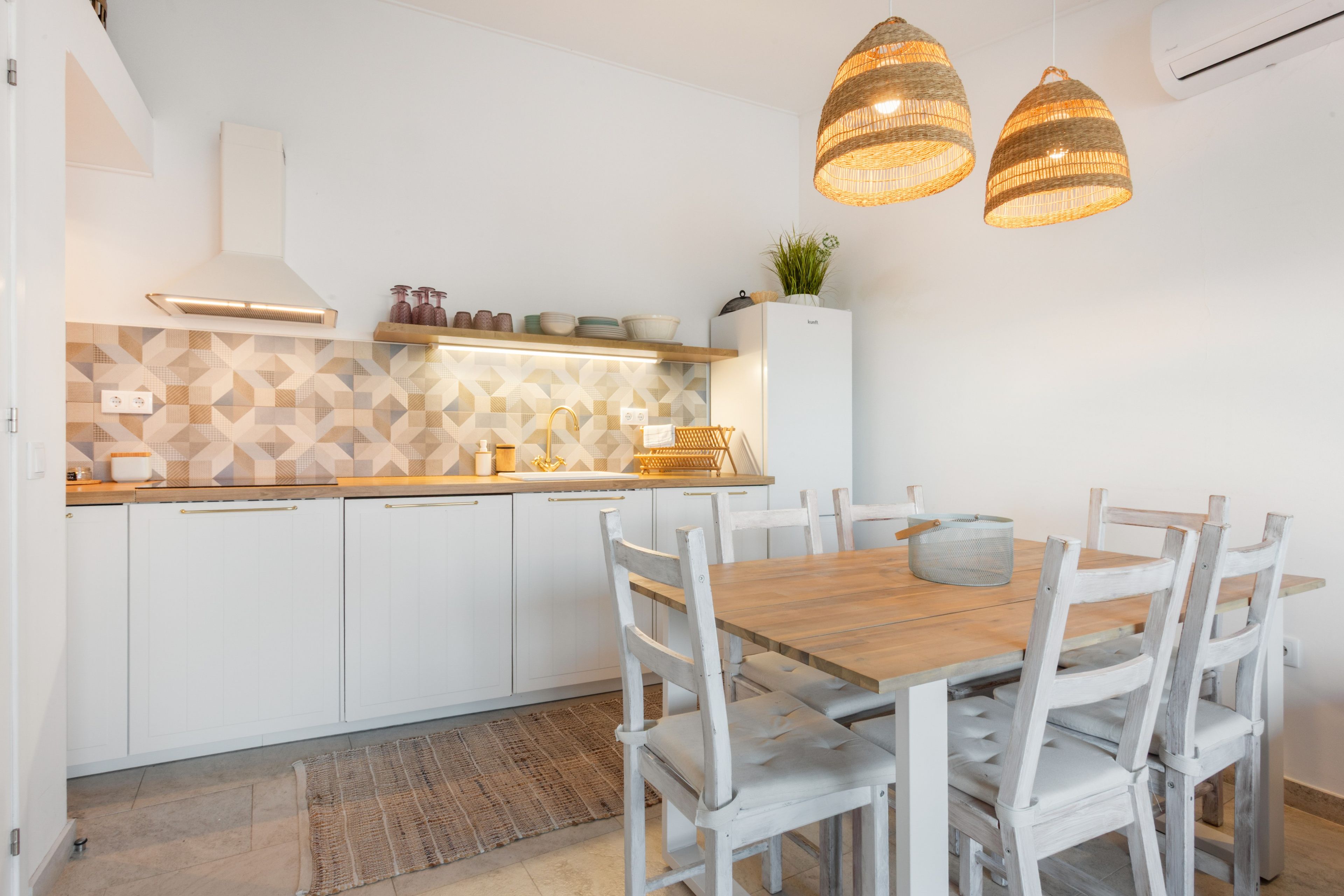 Eine moderne Küche mit weißen Schränken, einem Holztisch und zwei Pendelleuchten.