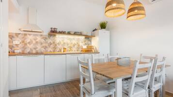 Eine moderne Küche mit weißen Schränken, einem Holztisch und zwei Pendelleuchten.