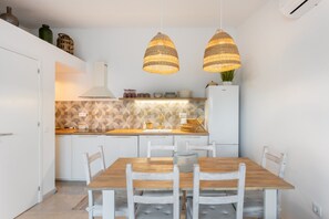 A modern kitchen with white cabinets, a wooden dining table, and two hanging wicker lamps.