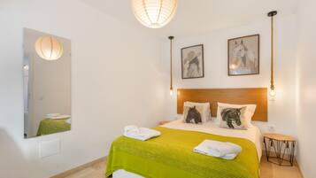 A hotel room with a bed, a mirror, two wall-mounted lights, and two framed pictures.