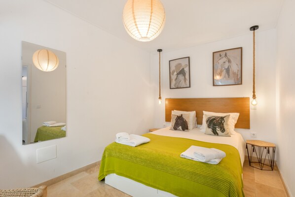 A hotel room with a bed, a mirror, two wall-mounted lights, and two framed pictures.