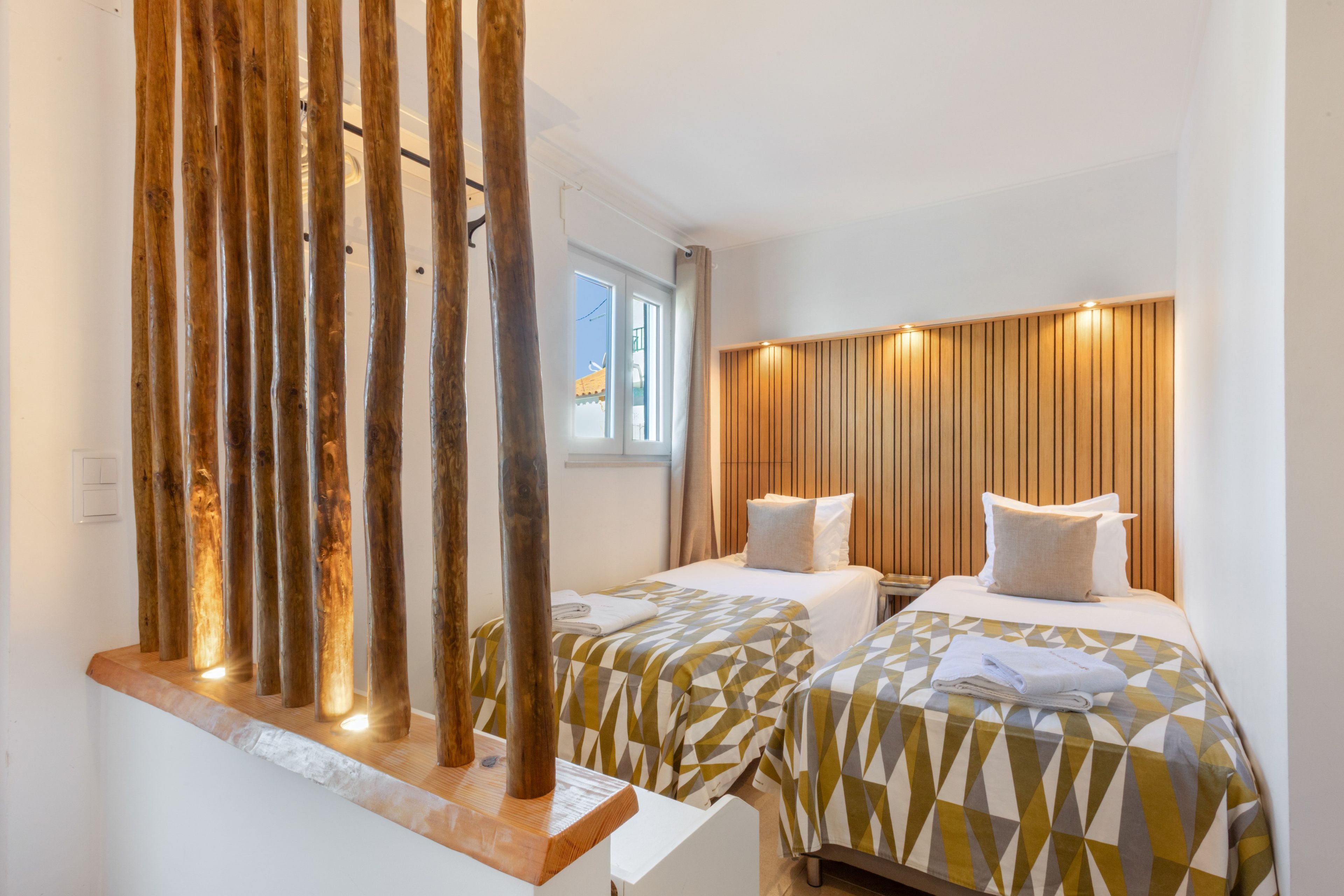 Une chambre d’hôtel avec deux lits, une tête de lit en bois et une fenêtre avec des rideaux.