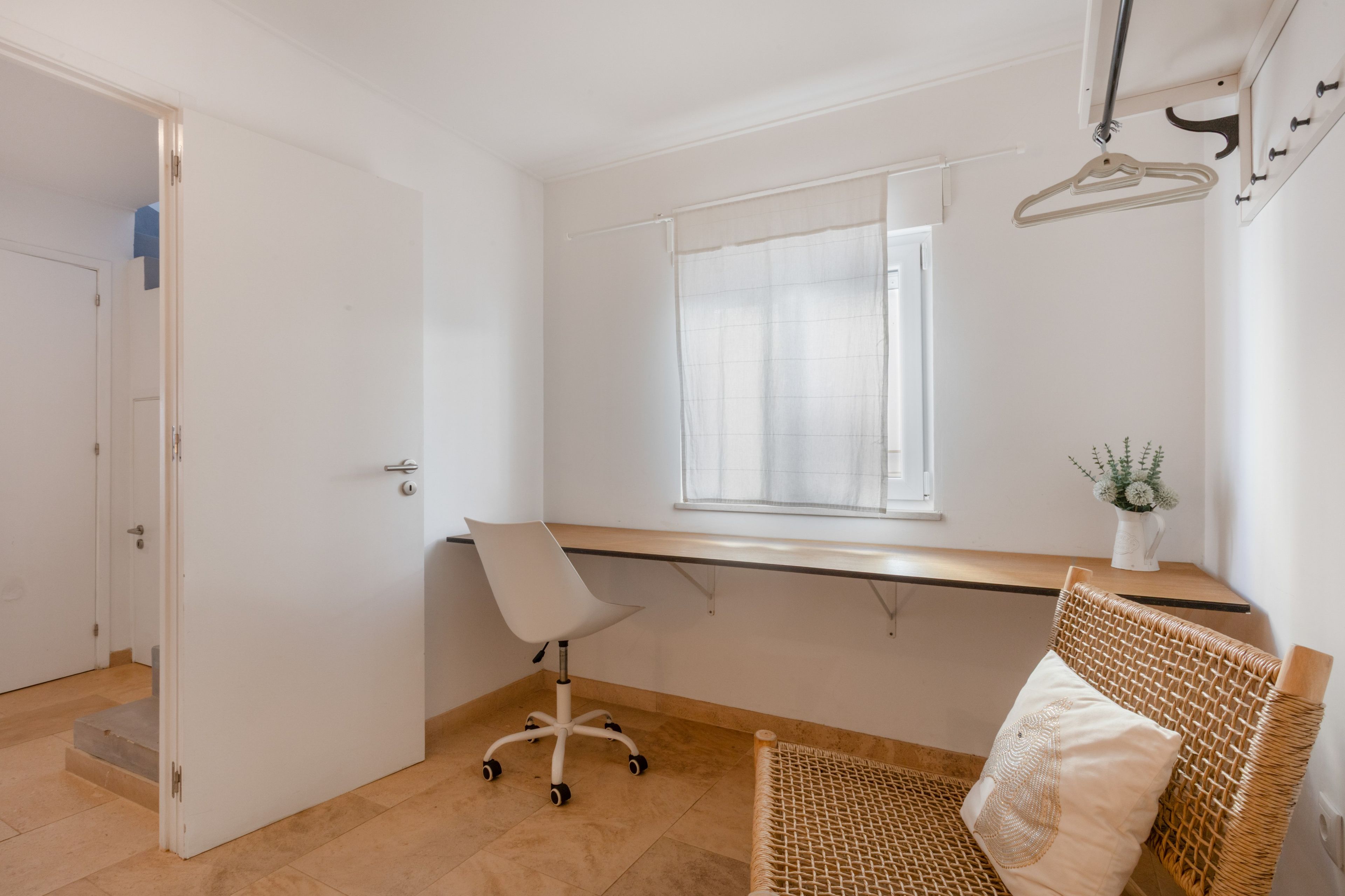 Une pièce avec un bureau, une chaise, une fenêtre, une porte et une petite plante.