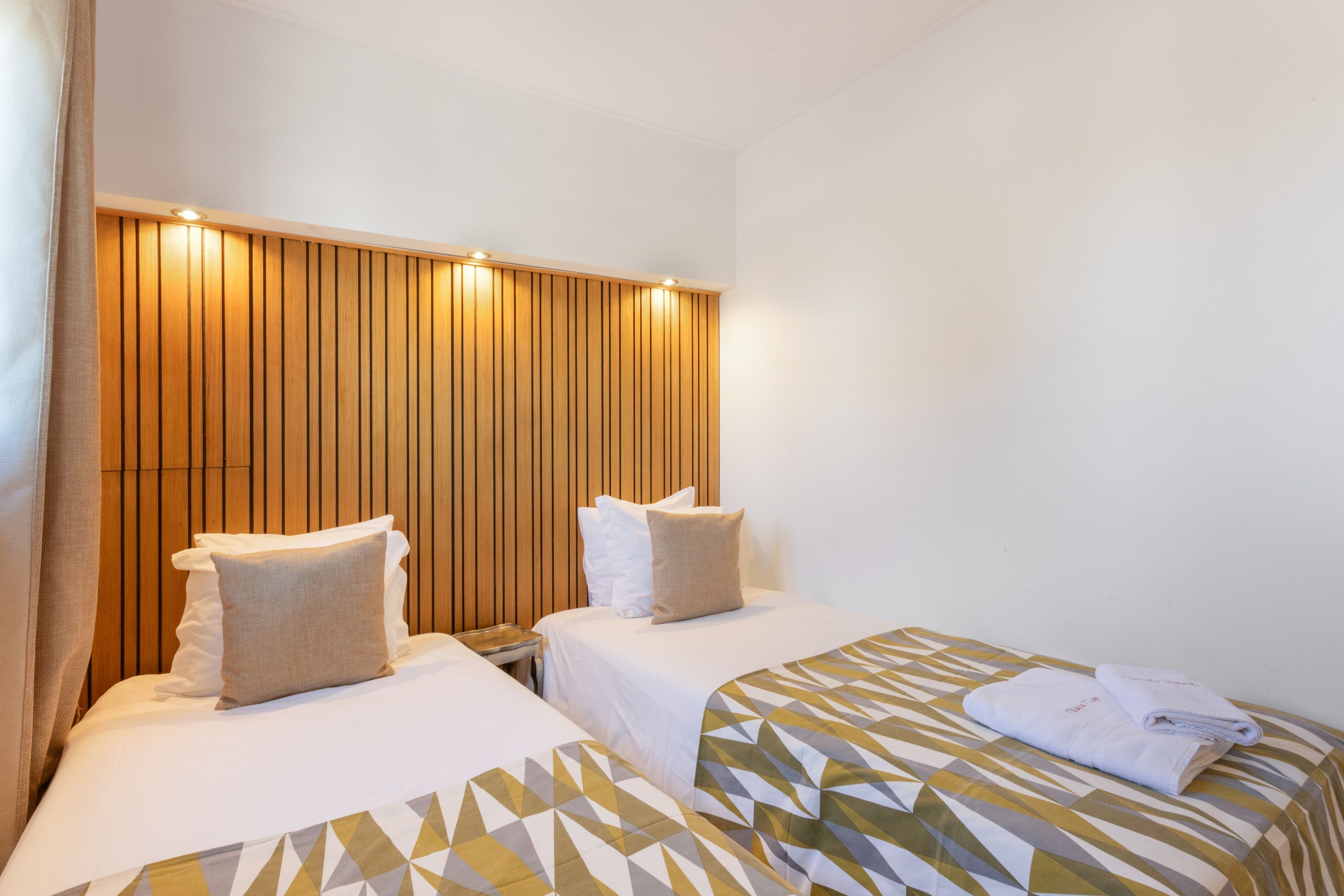 A hotel room with two beds, each with a pillow and a blanket.