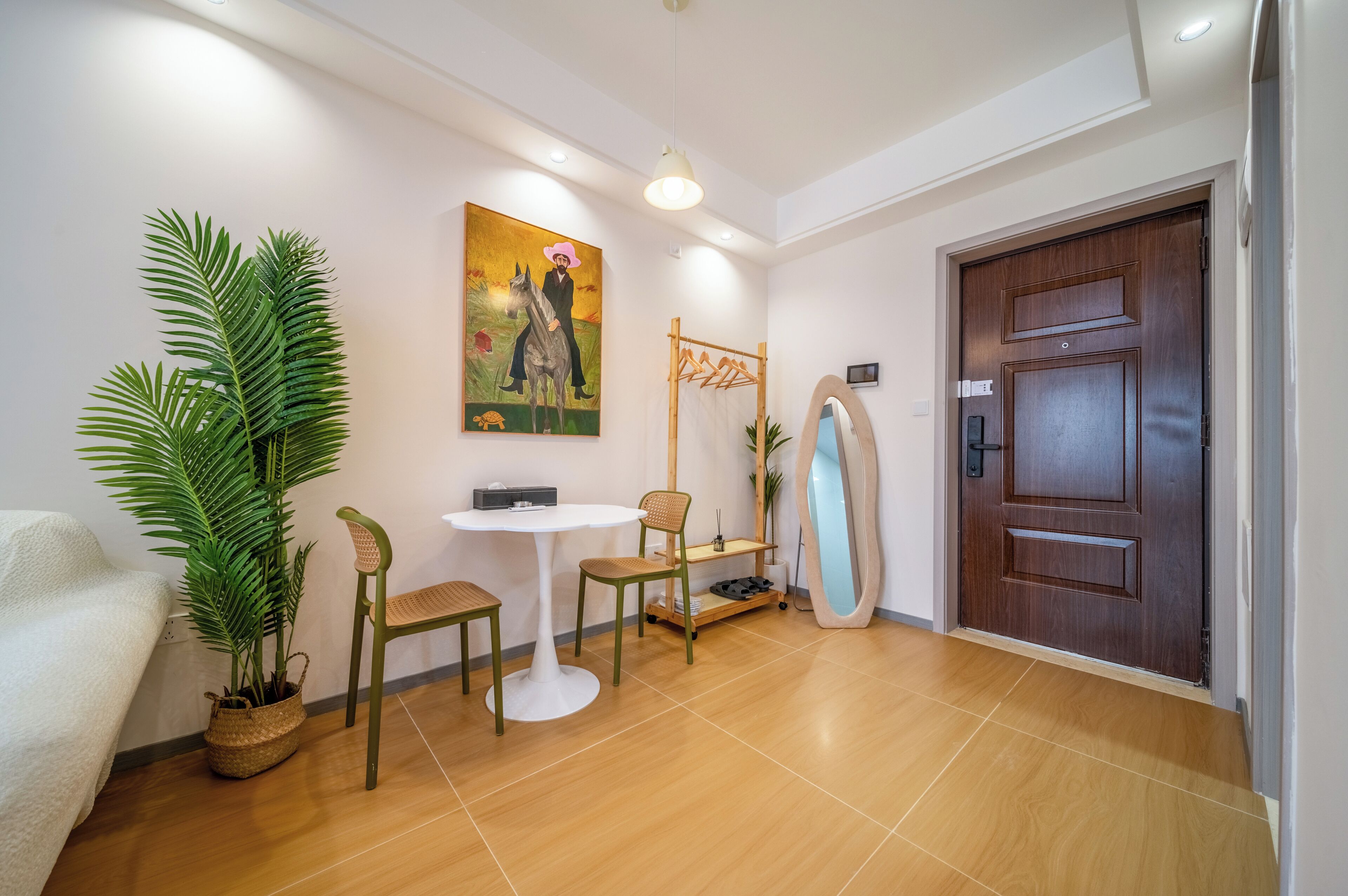 Une pièce avec un canapé blanc, une petite table ronde, deux chaises, une plante en pot, un tableau, un porte-manteau en bois et une porte.