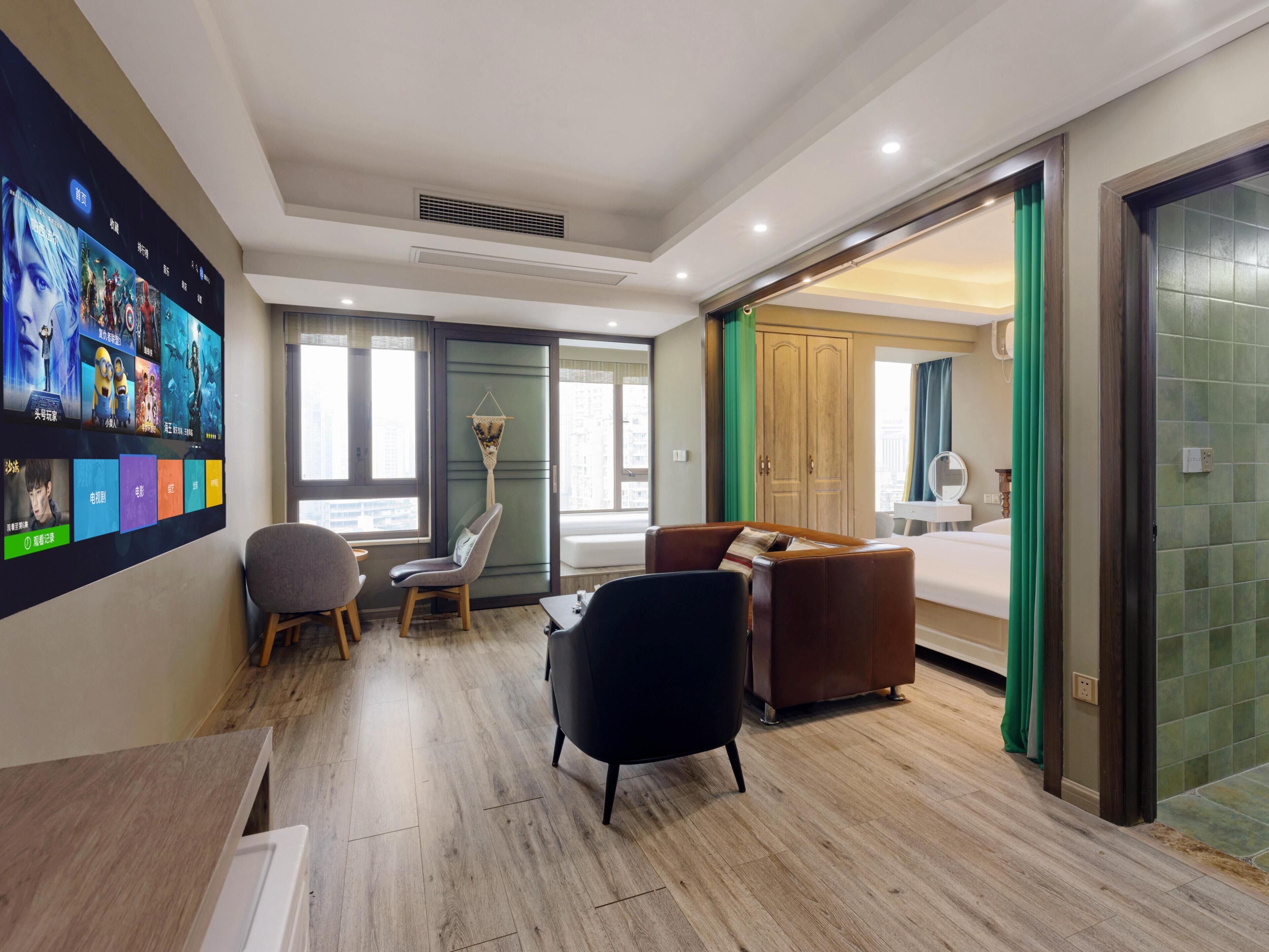A modern hotel room with a flat-screen TV, a sofa, a chair, a desk, and a bed.