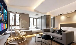 Habitació d'hotel moderna amb sofà, cadira penjant, llit, televisió i una finestra gran.