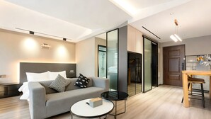 Een moderne woonkamer met een bank, een ronde salontafel, een eethoek met een houten tafel en stoelen, en een schuifdeur naar een douchegedeelte.