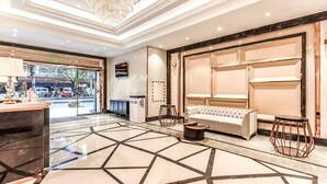 Een hotel lobby met een vloer met een geometrisch patroon, een bank, een salontafel, een kroonluchter en een receptiebalie.