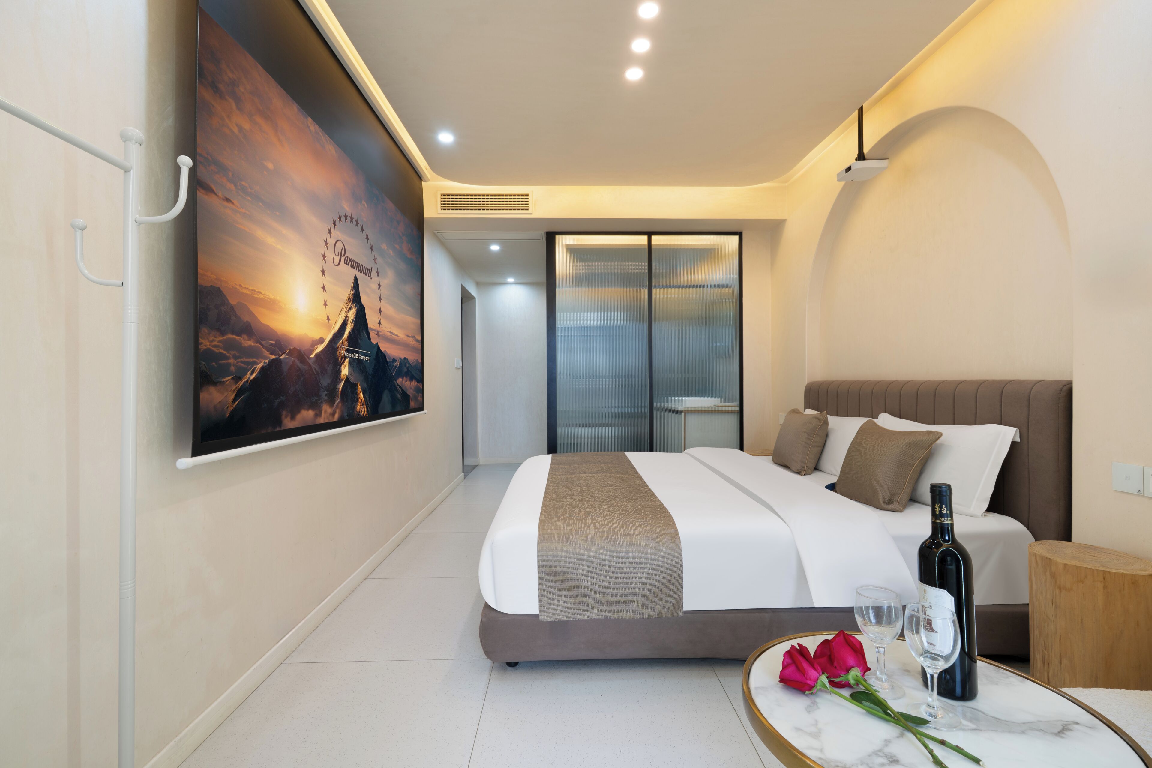 A modern hotel room with a large bed, a marble bedside table, a bottle of wine, and a framed picture on the wall.