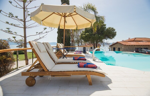 Un área junto a la piscina con sillones de descanso, una sombrilla y vistas al mar.