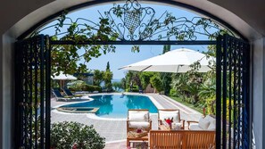 Piscina con sillas de descanso y sombrillas, rodeada de vegetación.