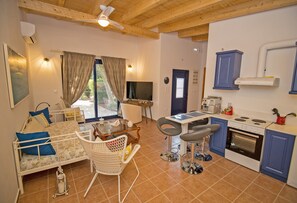 Una habitación con cama, televisión, mesa de comedor con sillas, kitchenette con estufa y ventilador de techo.