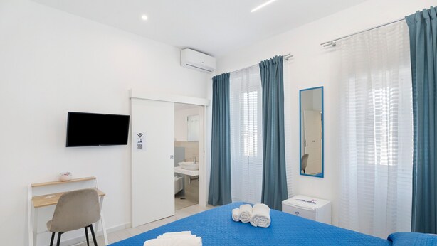 A hotel room with a bed, a desk, a chair, a TV, a bathroom, and a mirror. - Le Stanze In Centro - Deluxe Double Room (Naples)