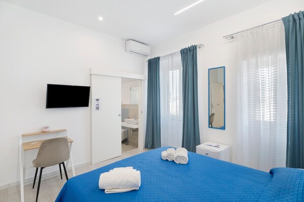 A hotel room with a bed, a desk, a chair, a TV, a bathroom, and a mirror. - Le Stanze In Centro - Deluxe Double Room (Naples)