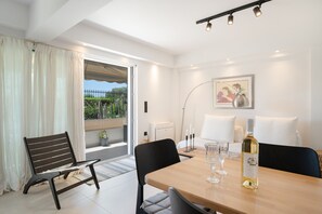 A modern room with a dining table, chairs, a bench, a bottle of wine, a framed picture, and a view of greenery outside. - Studio Apartment 'Athens-riviera in Front' with Sea View, Wi-Fi and Air Conditioning (Voula)