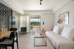 A modern room with a sofa, dining table, chairs, a coffee table, a decorative screen, and a view through a glass door. - Studio Apartment 'Athens-riviera in Front' with Sea View, Wi-Fi and Air Conditioning (Voula)