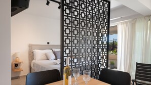 A hotel room with a bed, a dining table with a bottle and glasses, a decorative screen, and a view of the outdoors. - Studio Apartment 'Athens-riviera in Front' with Sea View, Wi-Fi and Air Conditioning (Voula)