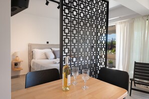 A hotel room with a bed, a dining table with a bottle and glasses, a decorative screen, and a view of the outdoors. - Studio Apartment 'Athens-riviera in Front' with Sea View, Wi-Fi and Air Conditioning (Voula)