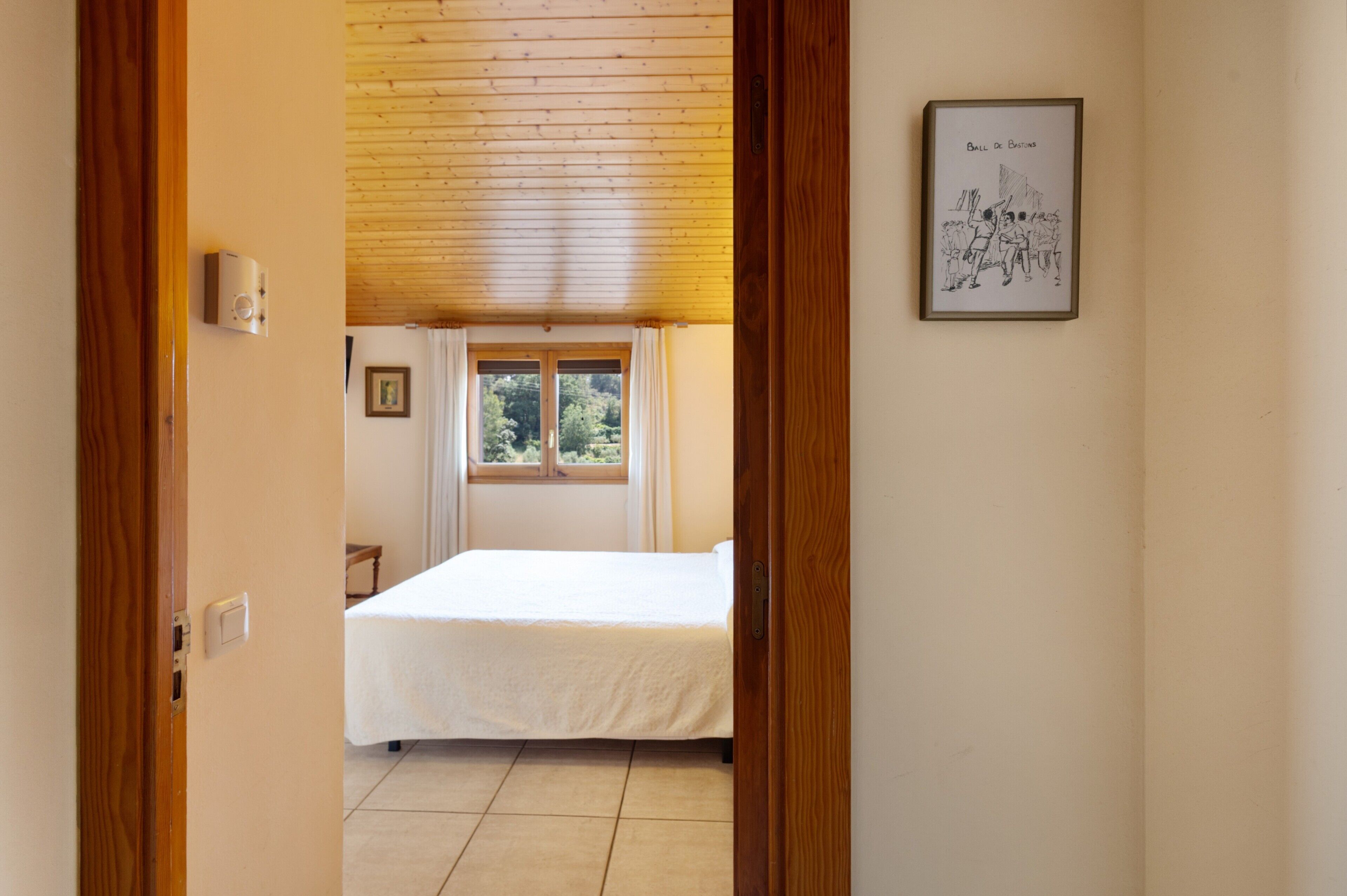 Una camera da letto con un letto, una finestra, un quadro incorniciato e un soffitto in legno.