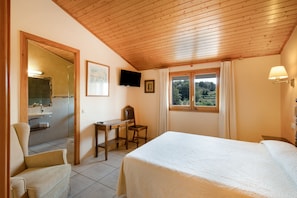 Un dormitorio con cama, escritorio, silla, televisor y ventana con cortinas.