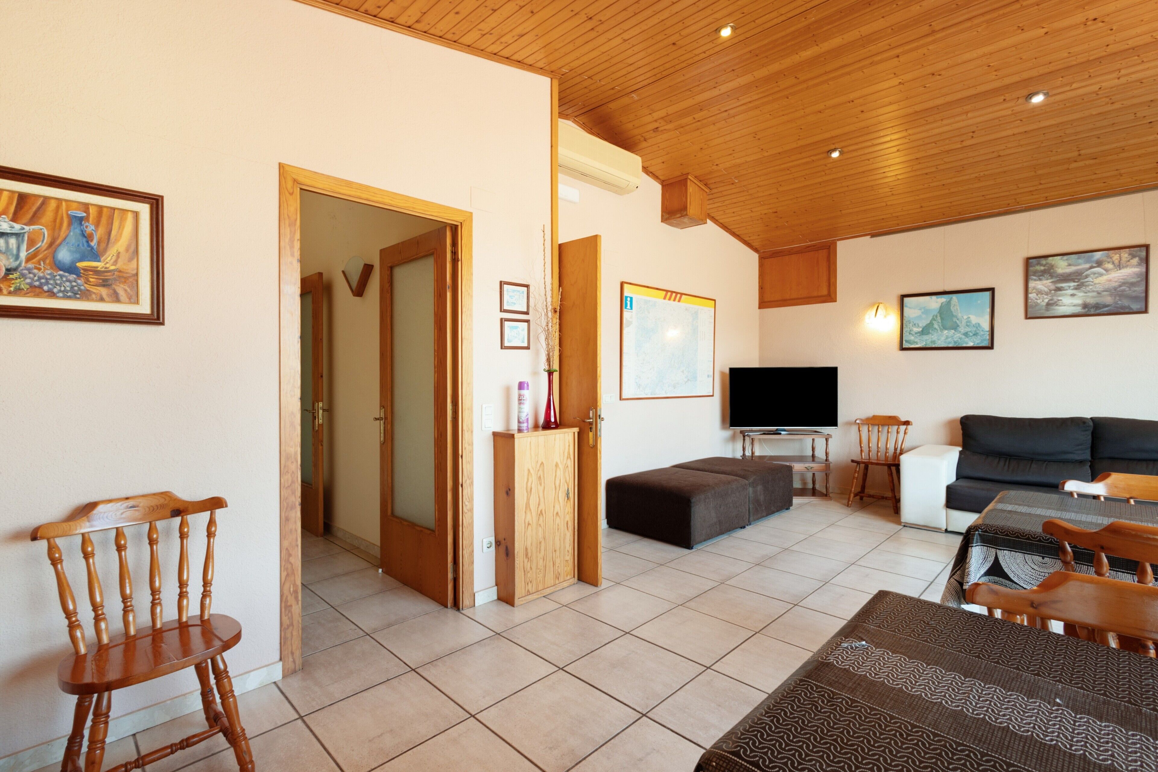 Un salon avec un plafond en bois, un téléviseur, un canapé, une table à manger avec des chaises et un meuble en bois.