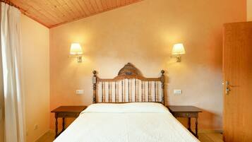 A bedroom with a wooden headboard, two bedside tables, a bed with a white bedspread, two wall-mounted lamps, and a wooden door.