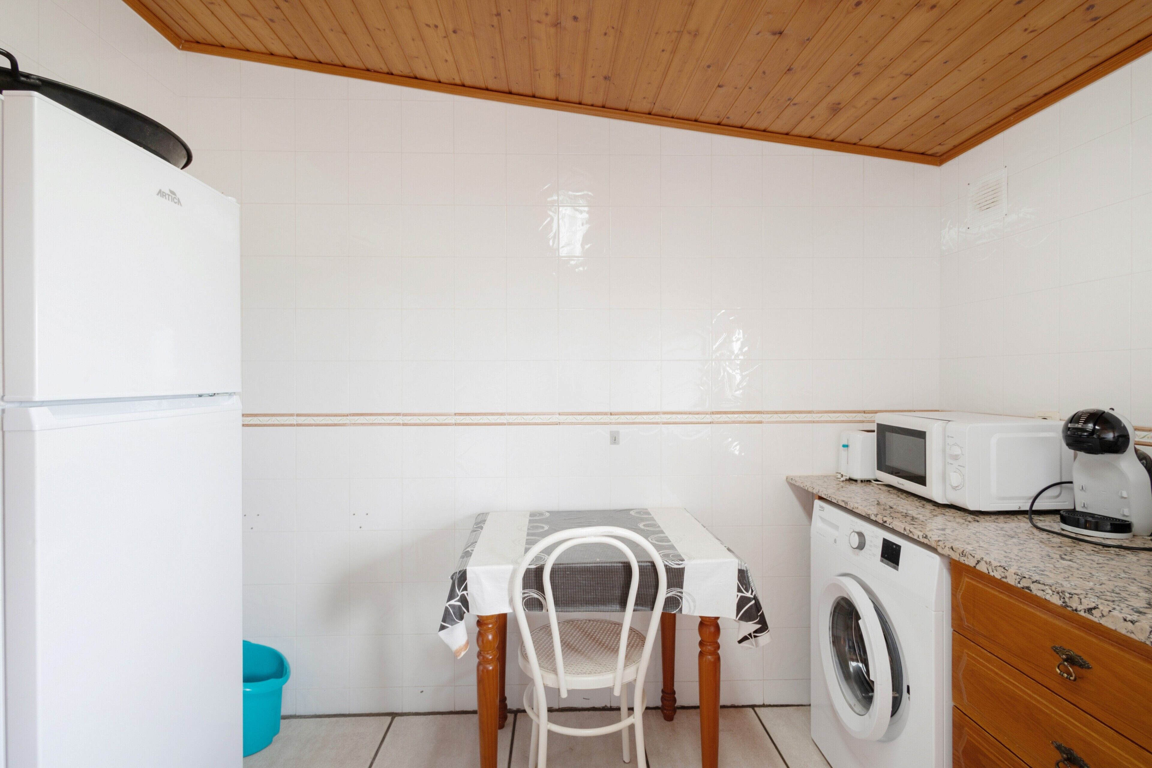 Una cocina compacta con lavadora, microondas y una mesa con una silla.