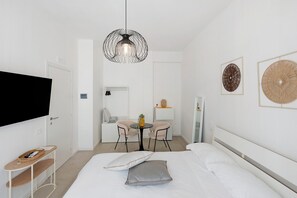 Quarto de hotel moderno com cama, televisão, uma pequena mesa com cadeiras e obras de arte nas paredes.