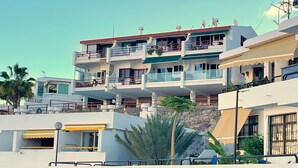 A multi-story residential building with balconies, a stone facade, and a clear sky. - Playa del Sol – Sea View Studio in Puerto Rico (Mogán)
