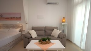 Una habitación moderna y luminosa con una cama, un sofá, una mesa de centro y una mesita auxiliar con un florero.