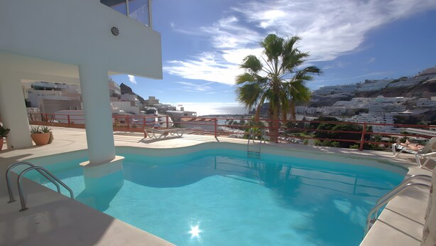 A swimming pool with a view of a coastal town and palm trees. - Playa del Sol – Sea View Studio in Puerto Rico (Mogán)