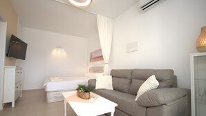 Una sala moderna con un sofá, una mesita pequeña, un televisor y una cama con una mesita de noche.