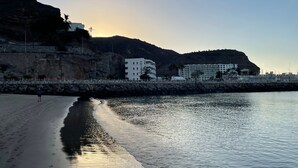 Escena costera con playa, acantilados rocosos y un edificio de varios pisos.