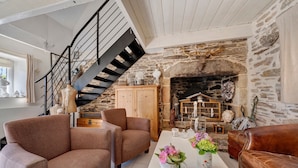 A cozy living room with a stone fireplace, a wooden staircase, and two brown sofas. - Maisonette Ti Arzou – 300m from the Beach (Le Conquet)