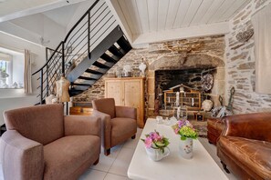 A cozy living room with a stone fireplace, a wooden staircase, and two brown sofas. - Maisonette Ti Arzou – 300m from the Beach (Le Conquet)