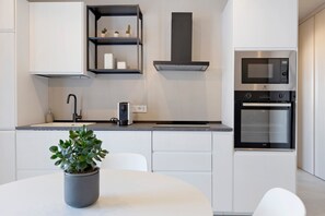 A modern kitchen with white cabinetry, a built-in microwave, oven, and a potted plant on the counter.