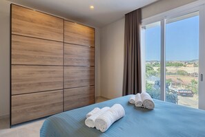 A hotel room with a large bed, a wooden wardrobe, and a view of the city through large windows. - Apartment 'Scirocco' with Balcony, Wi-Fi and Air Conditioning (Santa Flavia)