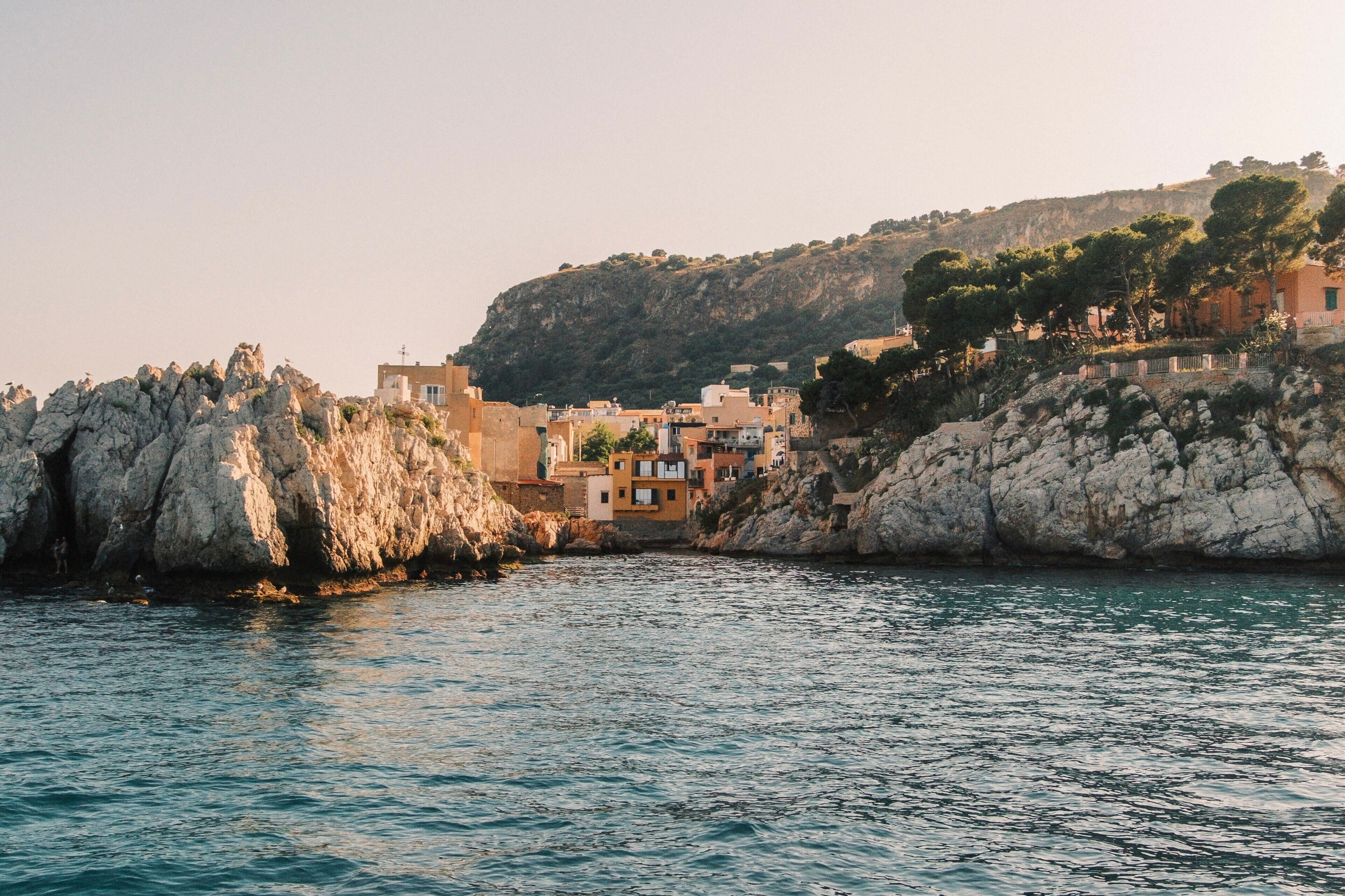 Un pueblo costero con edificios sobre acantilados rocosos y un mar tranquilo.