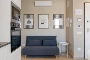 A modern kitchen with built-in appliances, a grey sofa, and a small white side table.