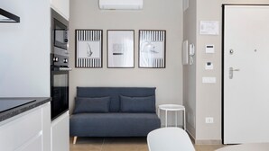 A modern kitchen with built-in appliances, a grey sofa, and a small white table. - Etesia Apartment with Balcony, Wi-Fi and Air Conditioning (Santa Flavia)