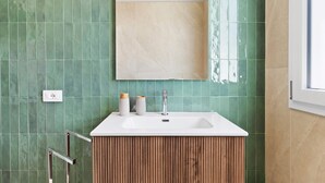 A bathroom with a white sink, green tiles, a wooden vanity, and a mirror above the sink. - Etesia Apartment with Balcony, Wi-Fi and Air Conditioning (Santa Flavia)